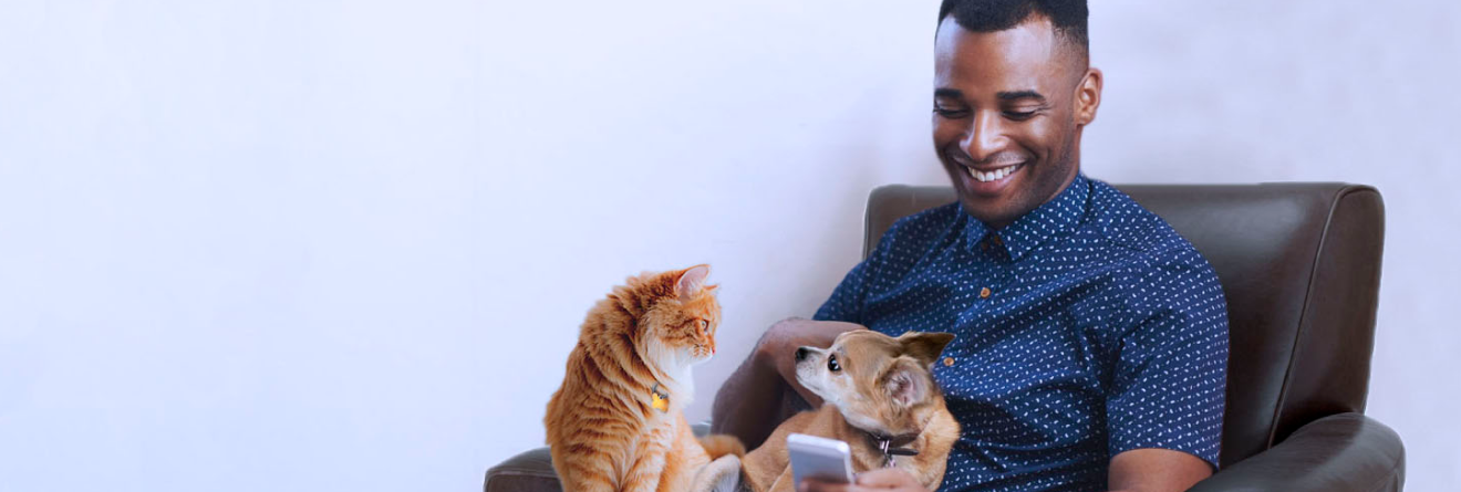 Man with cat and dog on lap smiling and looking at phone screen